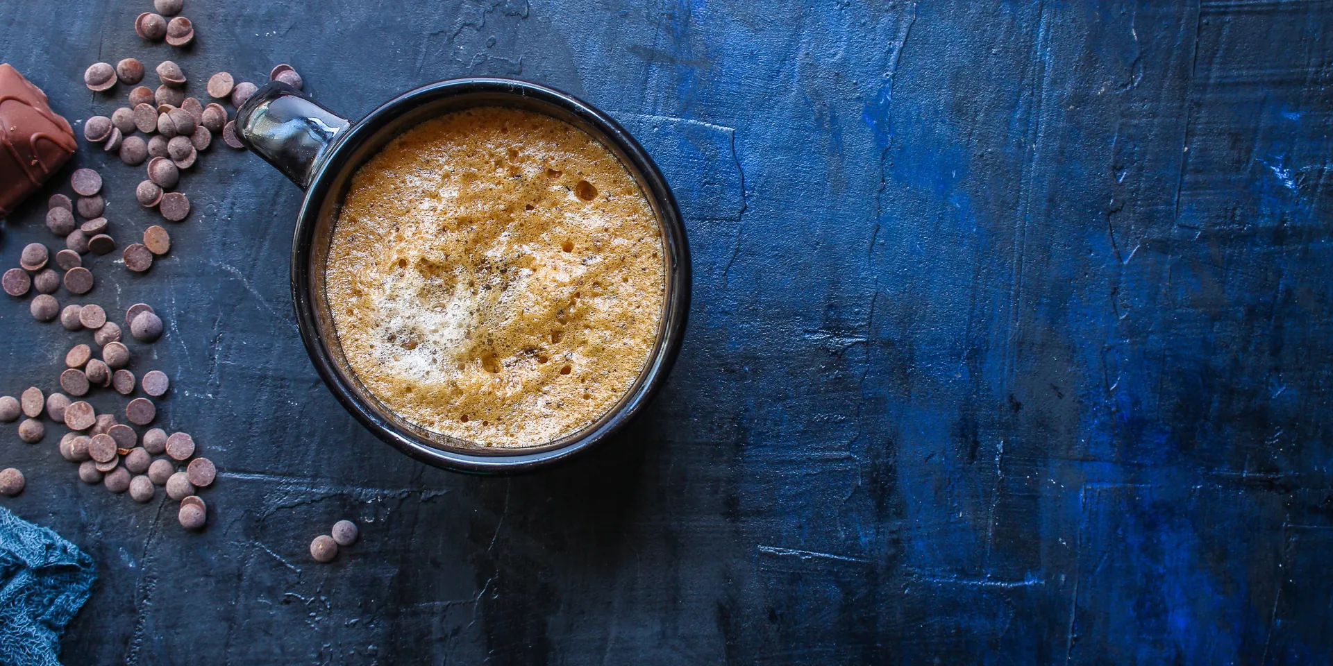 Top-down mocha in a dark mug on a blue surface with chocolate chips