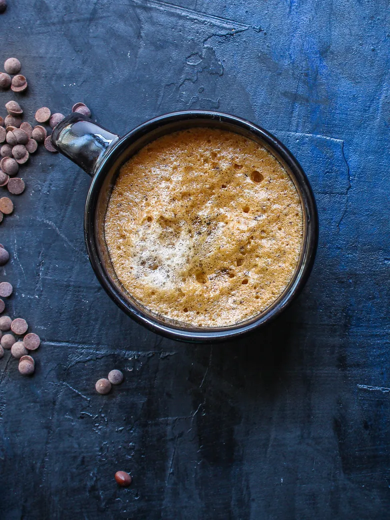 Top-down mocha in a dark mug on a blue surface with chocolate chips